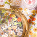 Orange, yellow and pink transparent flower stickers and leaf pieces heaped in a gold ornate frame tray