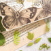 Fern and leaf stickers beside a large vintage butterfly illustration on a printed journal page