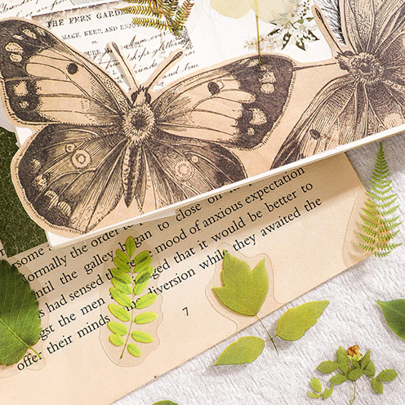 Fern and leaf stickers beside a large vintage butterfly illustration on a printed journal page