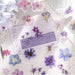 Purple and blue flower stickers placed on a journal page with newsprint and a blossom card