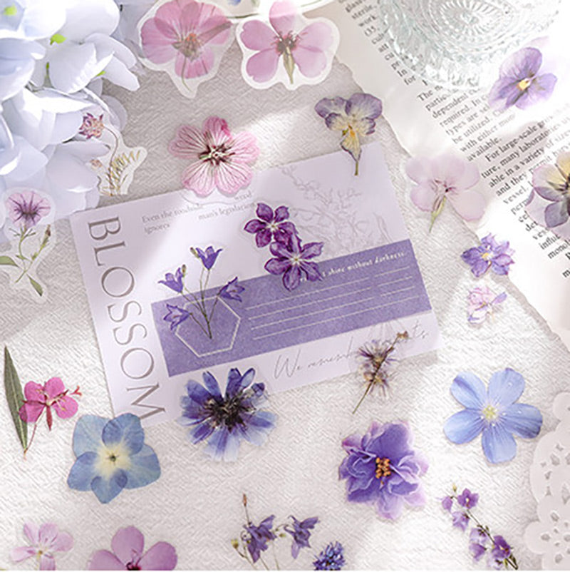 Purple and blue flower stickers placed on a journal page with newsprint and a blossom card