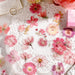 Pink pressed flower stickers arranged on a white lace doily beside a pink sticker box