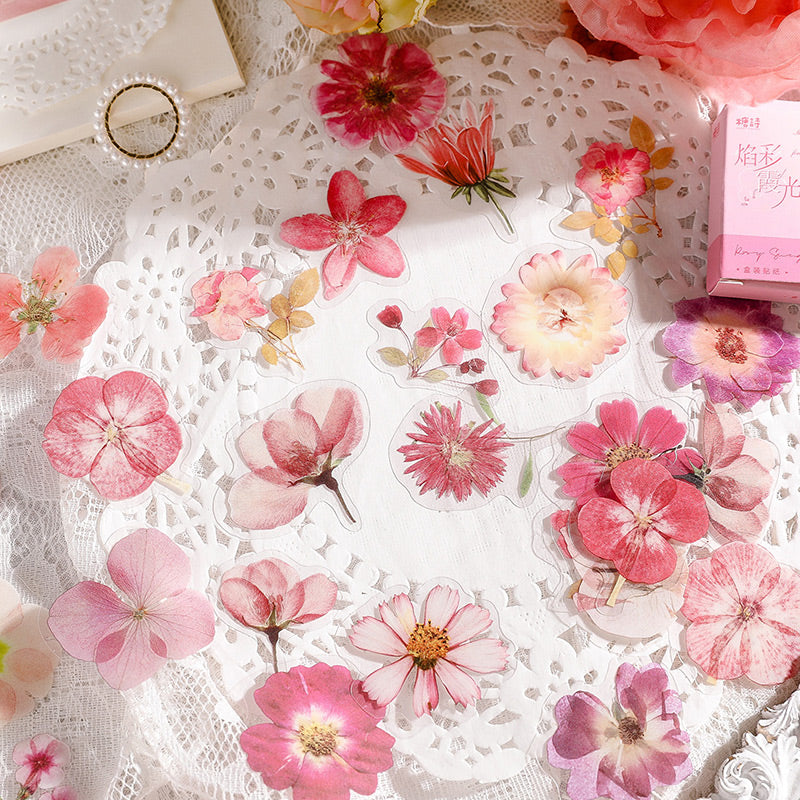 Pink pressed flower stickers arranged on a white lace doily beside a pink sticker box