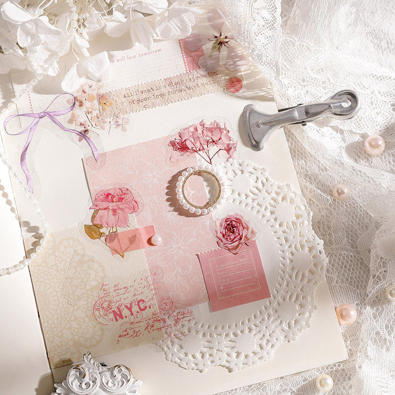 Pink flower stickers layered on a vintage journal page with pink paper, a metal clip and pearls