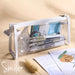 Clear triangular zipper pencil case with white trim, filled with pens and stationery
