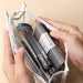 Hands holding open a clear triangular zipper pencil case packed with pens and washi tape