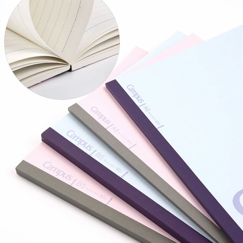 Fanned pink, blue, and grey Kokuyo Campus notebooks with inset of cream pages and dotted blue lines.