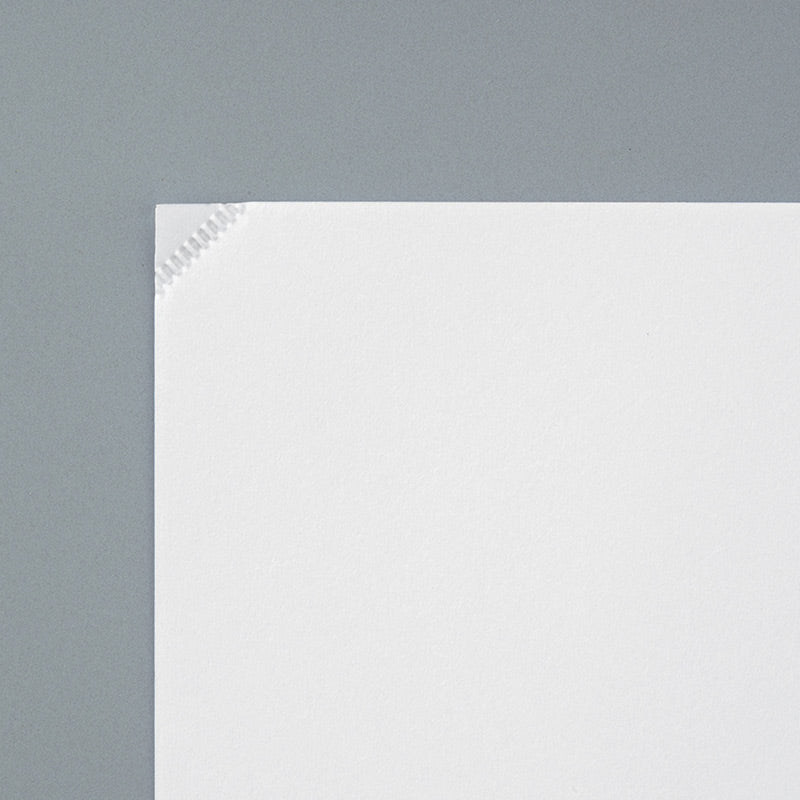 Close-up view of a pale white KOKUYO Harinacs Press Stapleless Stapler resting on a clean white sheet of paper, highlighting the pressed corner binding mark.