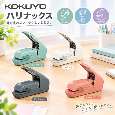 Four Harinacs stapleless staplers in teal, white, dark grey and salmon pink on a wooden desk beside notebooks
