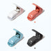 Color chart of four stapleless staplers in white, coral pink, light blue and dark grey with their levers raised