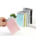 Pink, blue, and yellow memo pads displayed on a desk beside a plant