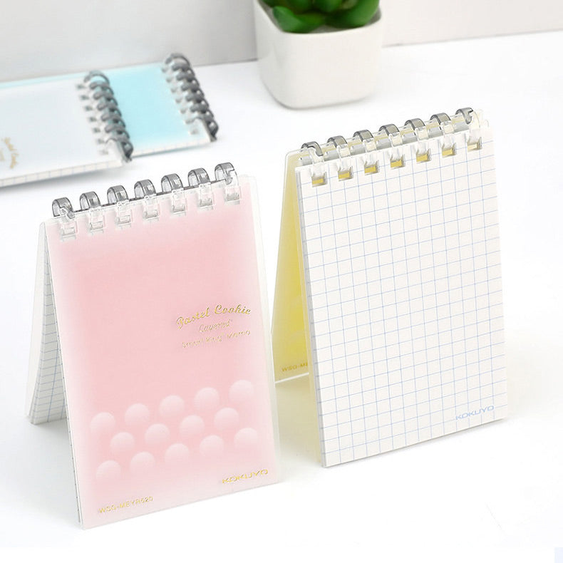Two ring-bound memo pads open flat on a desk beside a small plant