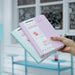 Hands holding Pale Purple and Pale Blue Paperideas 2027 A5 hardcover planners with elastic bands and belly bands