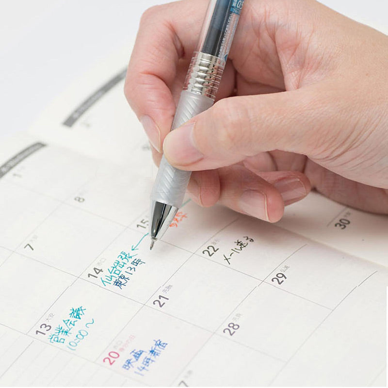 Hand writing colorful notes in a monthly planner with a 0.5mm EnerGel Infree gel pen