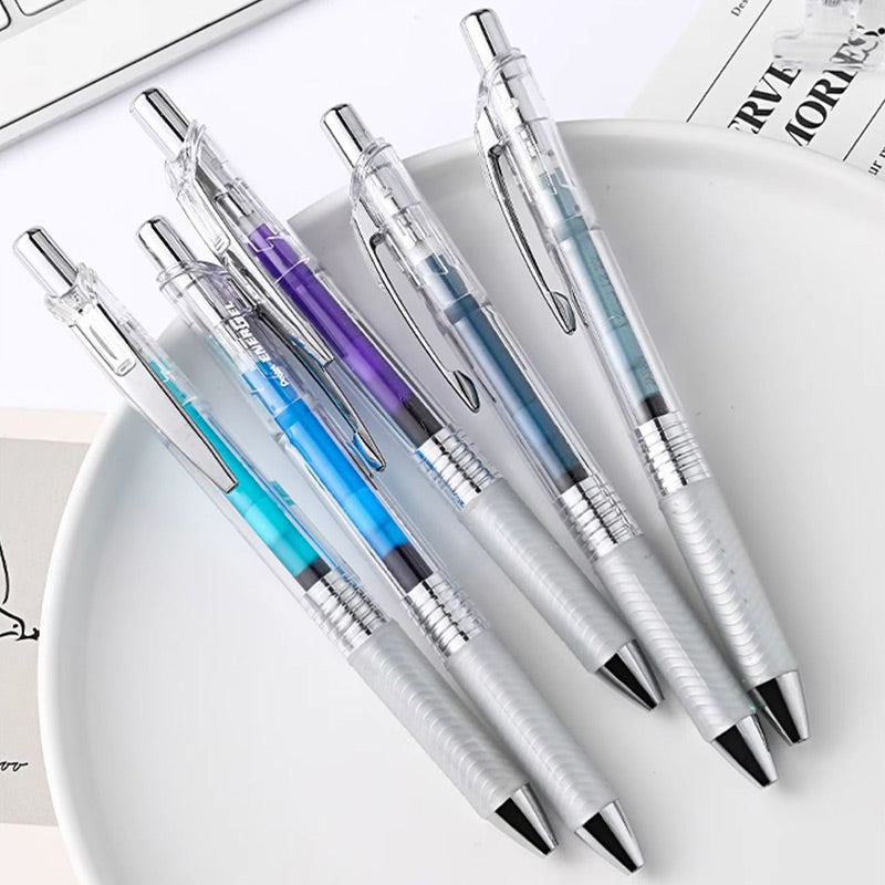 Five transparent EnerGel Infree gel pens with violet, blue, turquoise and gray ink resting on a white plate