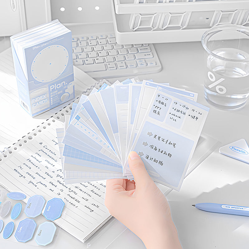 Hand fanning out blue index cards with schedule notes beside the storage box on a study desk