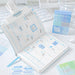 An open planner with a weekly calendar layout and blue sticky notes, shown on a white desk with a keyboard, glass, and a small blue package labeled Plan-Plan.
