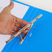 Hand lifts silver spring bar above blue folder base plate marked 8 cm between posts.