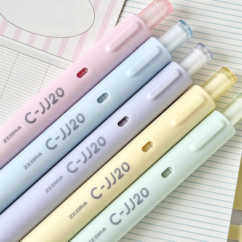 Five pastel C-JJ20 gel pens in pink, blue, purple, yellow and green resting on lined notebook paper