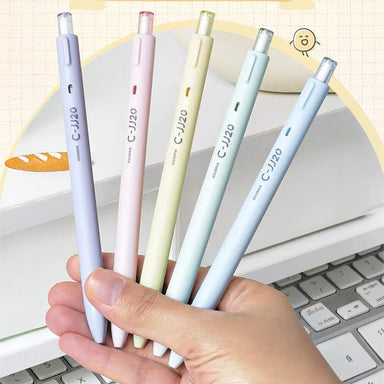 Hand holding five pastel purple, pink, yellow, green and blue C-JJ20 gel pens above a laptop keyboard