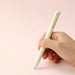 Hand holding a cream Signo RT1 gel pen with an extended rubber grip against a soft pink background